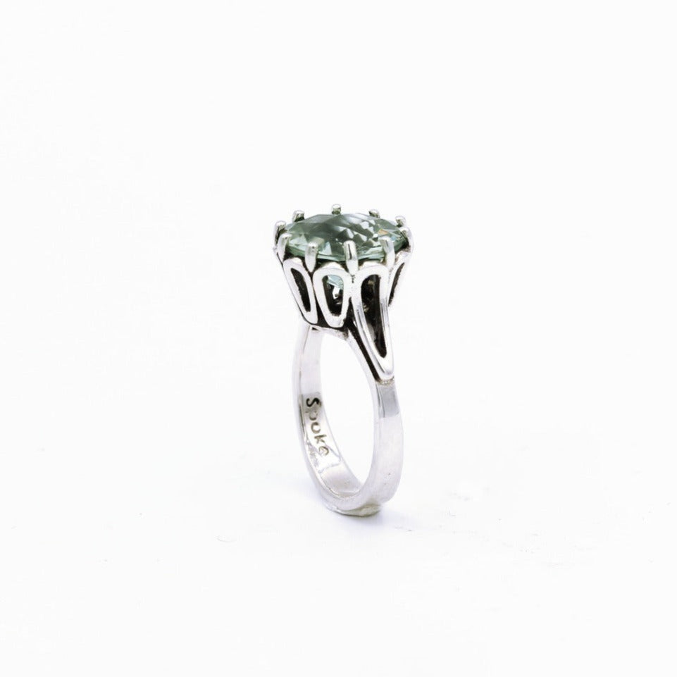 A silver ring featuring a green amethyst gemstone, set in an intricate crown setting.