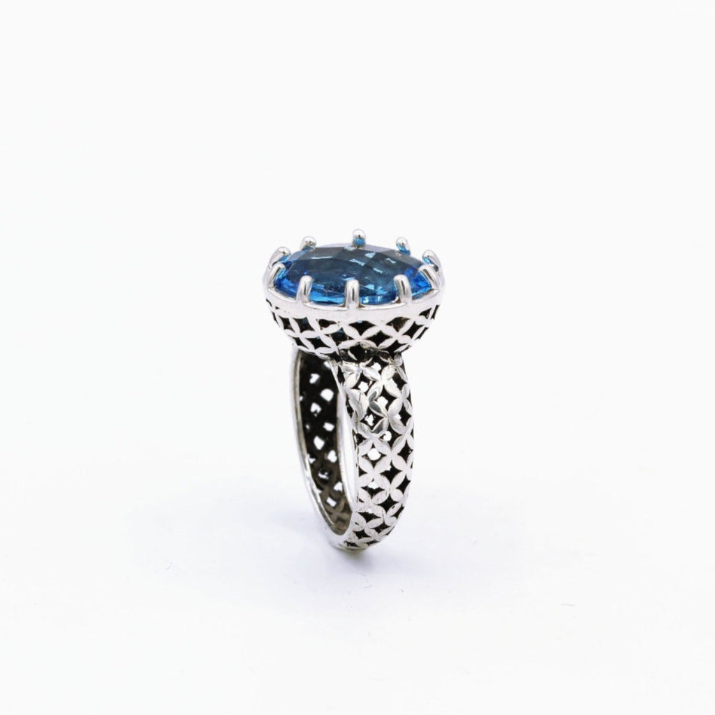 A sterling silver ring with a faceted blue topaz gemstone, featuring intricate metalwork on the band.