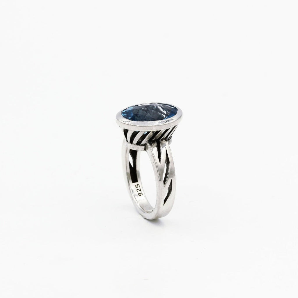 A blue topaz gemstone ring set in a sterling silver band, viewed from the side, showing the ring's profile.